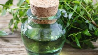 A container of myrtle oil with fresh leaves on a wooden table