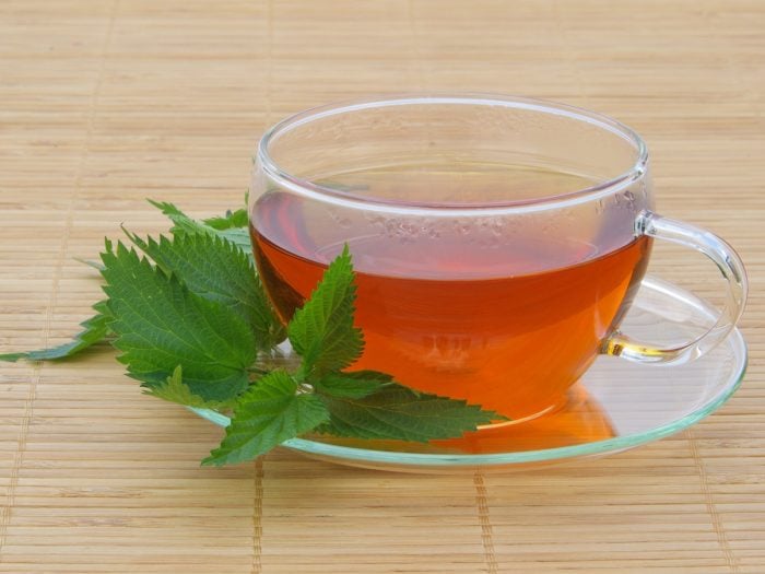 A cup of nettle tea with fresh nettle leaves