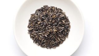 A flat lay picture of nigerseeds kept in a white plate against a white background
