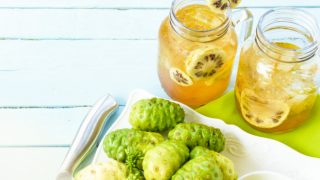 2 glasses of noni juice with noni fruits on a light blue background