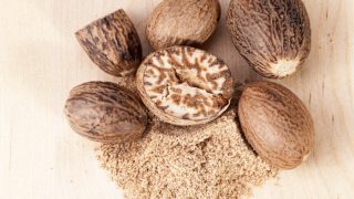 A close-up view of whole nutmegs and nutmeg powder on a wooden background