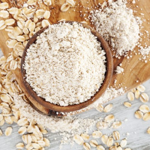 Wholegrain oat flour in spoon with oat flakes on wooden table