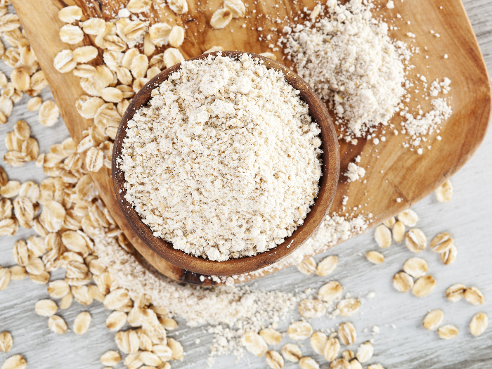 Wholegrain oat flour in spoon with oat flakes on wooden table