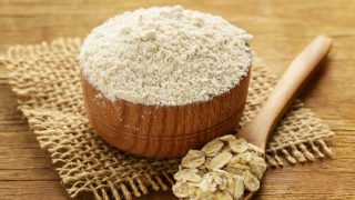 Natural organic oat flour in a wooden bowl and oats on a wooden spoon