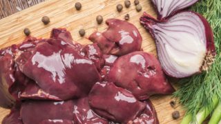 Offal on a wooden board, with peppercorns, halved onion, and herbs