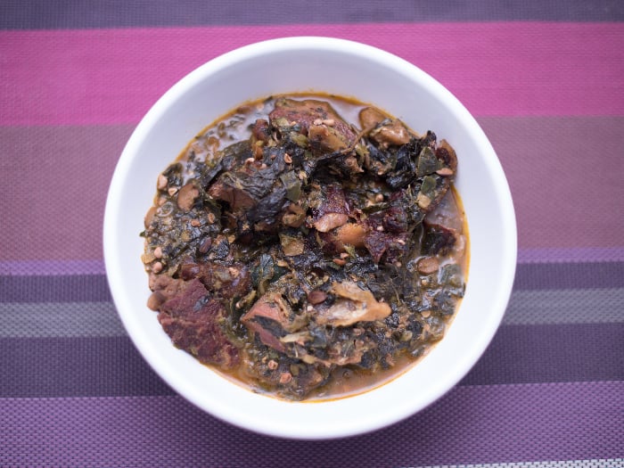 A white plate of Ogbono soup with mixed okra, dried fish and and bush meat on a purple mat