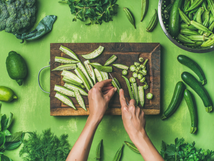 A person cutting okra on a wooden board