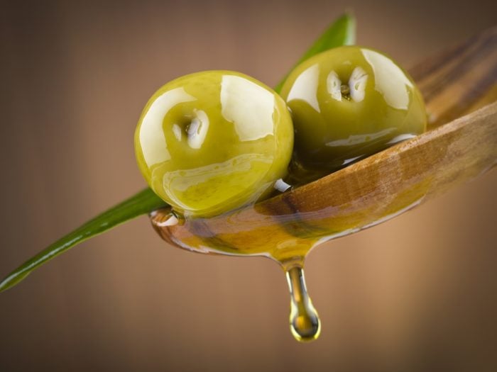 Olives on a wooden spoon with brine falling in a drop form