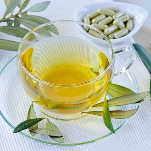 olive leaf tea in a glass cup and saucer with olive leaves and a dish of supplements