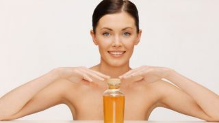 A woman with bare shoulders, smiling while touching an oil bottle