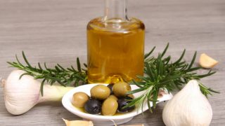 Olive oil bottle with herbs, whole garlic, green onion and olives