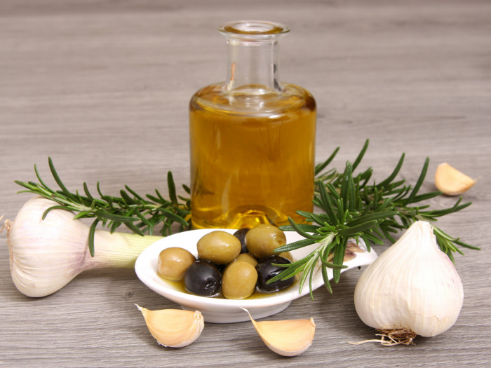 Olive oil bottle with herbs, whole garlic, green onion and olives