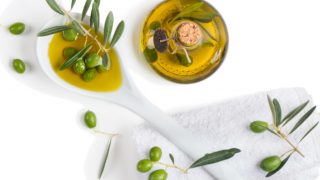 Olive oil bottle and a spoon of olive oil, with fresh olives and olive leaves