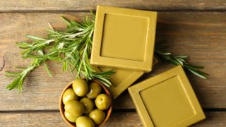 Olive oil soap bars next to a bowl of green olives and rosemary sprigs