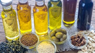 Different varieties of oil next to bowls of sunflower seeds, olives, sesame seeds