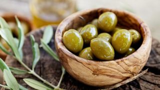 A wooden bowl of fresh olives on a wooden plank