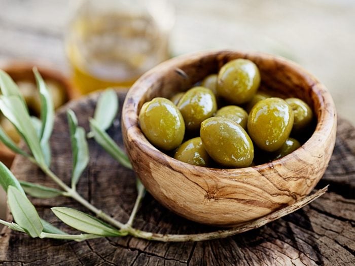 A wooden bowl of fresh olives on a wooden plank