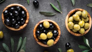 Three bowls of black and green olives on a black background decorated with leaves