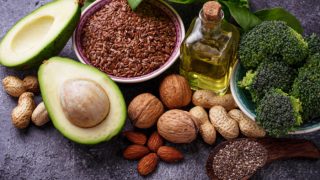 Various omega 6-rich foods like avocado, seeds, walnuts, almonds, and broccoli on a table