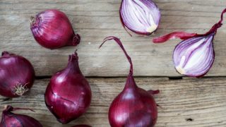 Whole and halved fresh onions on a wooden table