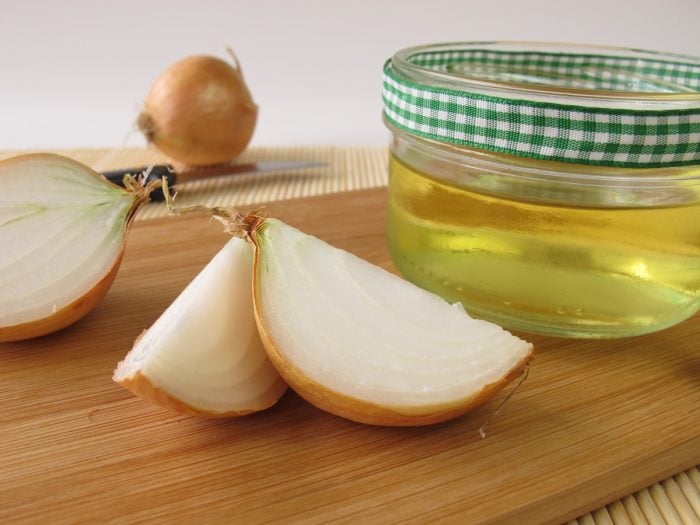 Onion juice in a glass container with onion wedges and whole onions