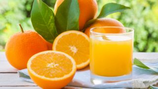 A close-up shot of a glass filled with fresh oranges kept beside oranges against a scenic background
