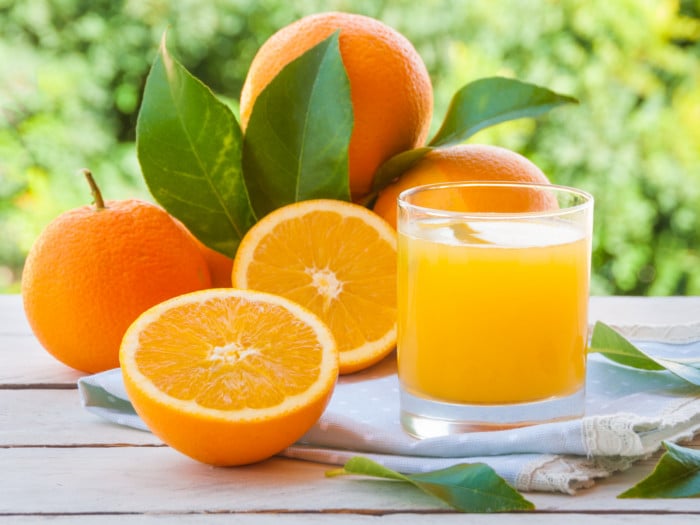A close-up shot of a glass filled with fresh oranges kept beside oranges against a scenic background