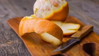 An orange peel, a knife and a partially peeled orange on a wooden board on a wooden surface
