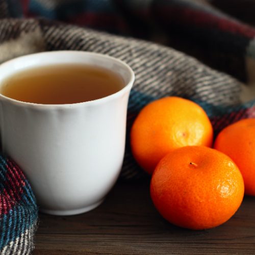 A cup of tea with a woolen scarf and oranges next to it.