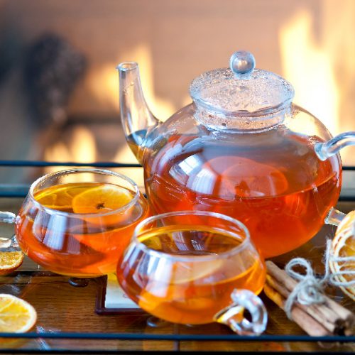 A glass tea set with orange-flavored tea, with a fire in the fireplace in the background