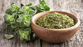 Fresh oregano herb and a wooden bowl of dried oregano on a wooden table