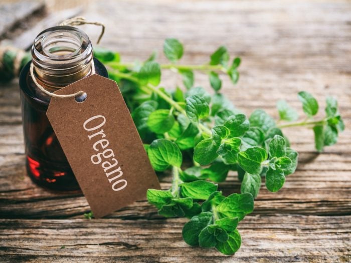 A bottle of oregano oil with oregano leaves on a wooden table