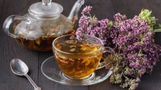 A jar and mug of oregano tea with fresh flowers on a wooden table