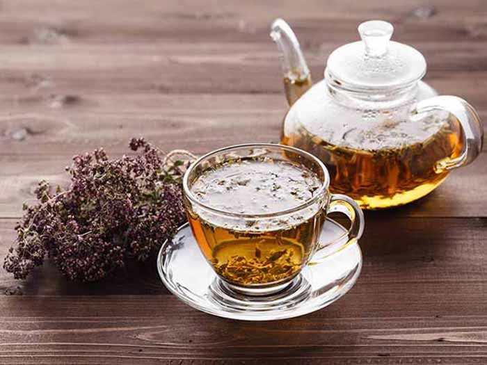 Oregano tea kept in a teapot next to a cup of oregano tea, on a wooden platform