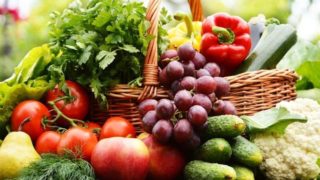 Basket of fresh organic foods (cilantro, tomatoes, red and yellow bell peppers, cucumbers, cauliflower, apples, pears, grapes, and okra)