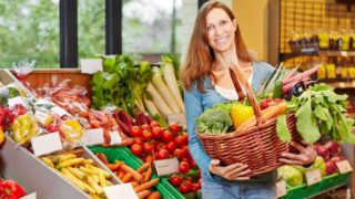 A woman holding a basket full of vegetables in a vegetable store