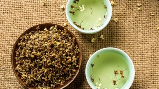 Flatline view of two bowls of water topped with osmanthus flowers and a big bowl of osmanthus on a burlap cloth.