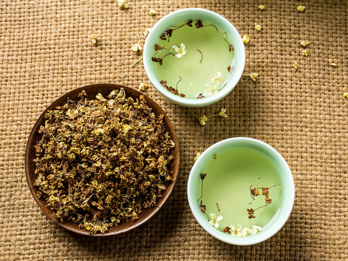 Flatline view of two bowls of water topped with osmanthus flowers and a big bowl of osmanthus on a burlap cloth.