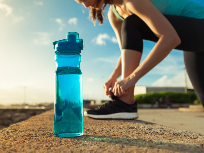 A woman in gym clothes tieing her shoelaces, with a bottle of water on the side