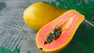 A whole papaya and a half-ripe papaya with leaves on a table
