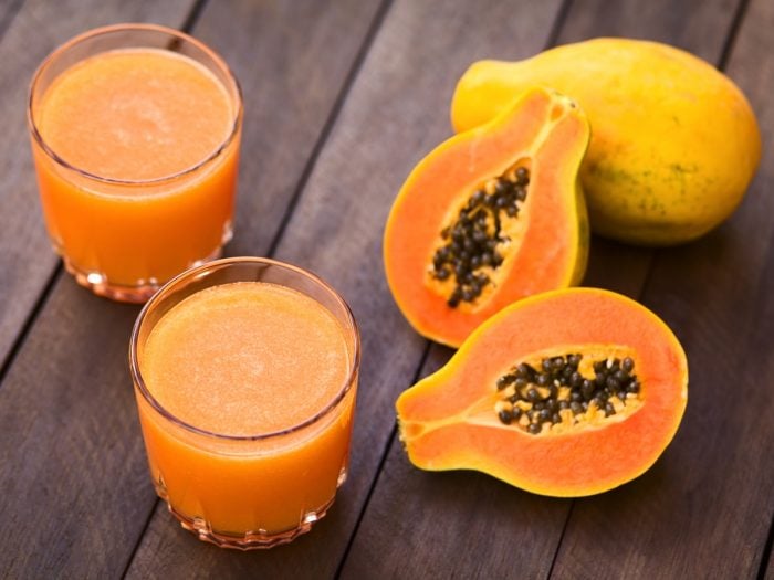 Two glasses filled with papaya juice kept next to the papayas on top of a wooden table