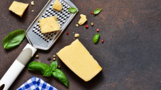 Flatlay pic of a black of cheese, grater, and basil leaves with a checked napkin on a slate surface