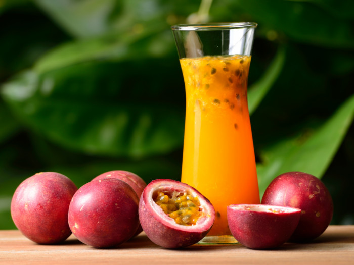 A glass of fresh passion fruit juice kept next to ripe passion fruits atop a table