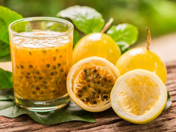 A glass of fresh passion fruit juice with whole and halved passion fruits on a wooden table