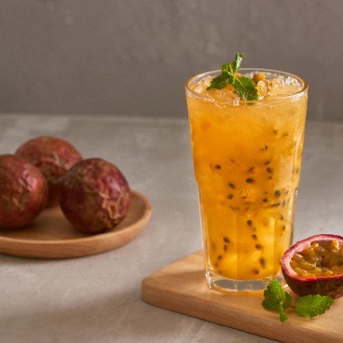 A glass of passion fruit juice kept next to passion fruits atop a table