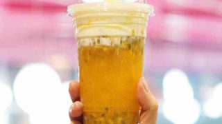 A hand holding a glass of passion fruit tea against a pink background