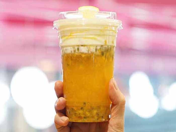 A hand holding a glass of passion fruit tea against a pink background