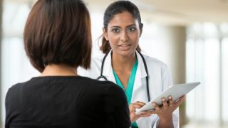 A doctor with a stethoscope and a clipboard, talking to a patient