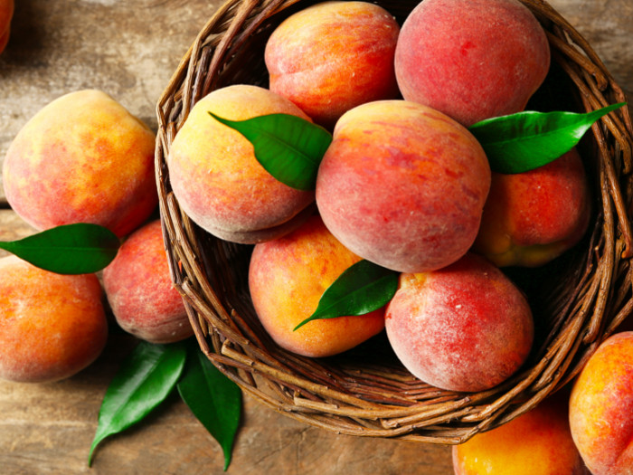 Ripe peaches in a basket on a wooden background