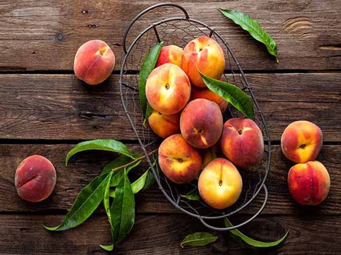 Peaches on a wooden counter with peach leaves